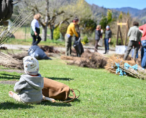 Kind sitzt im Gras, im Hintergrund Menschen bei inklusivem Sozialprojekt im Grünen, Frühling