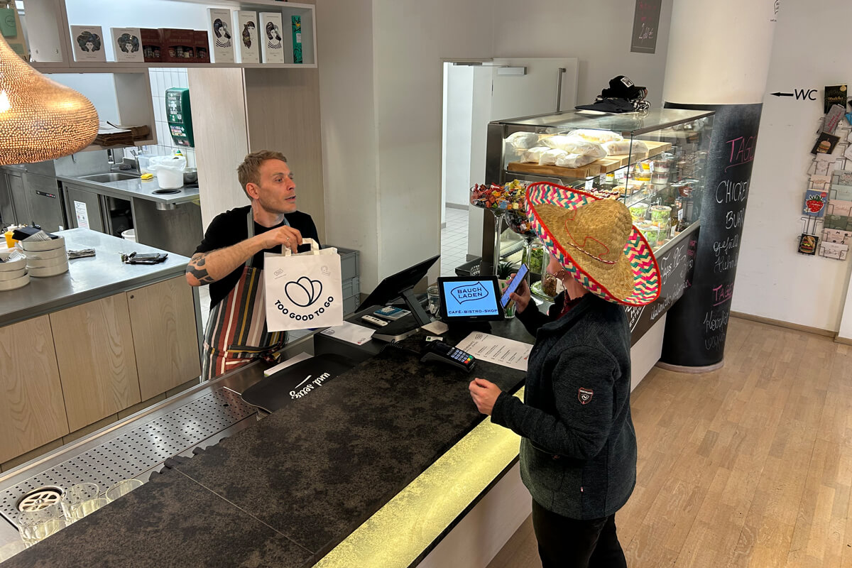 Mitarbeiter reicht Kundin in Sombrero Essen in sozialem Bistro mit Arbeitsintegration