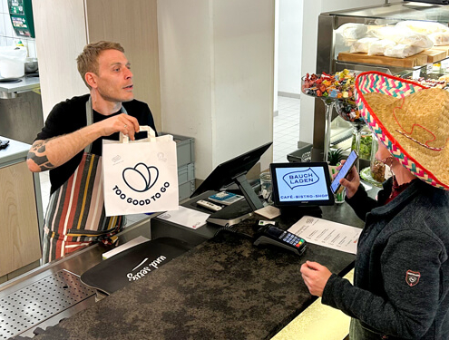 Mitarbeiter im Sozialunternehmen unterstützt Kunden im Café zur Arbeitsintegration und Teilhabe
