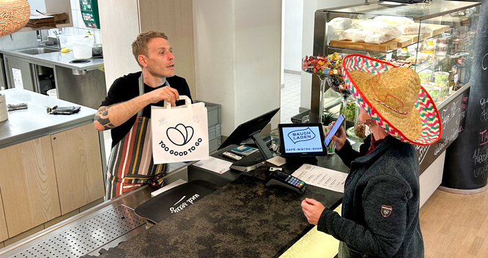 Mitarbeiter im Sozialunternehmen unterstützt Kunden im Café zur Arbeitsintegration und Teilhabe