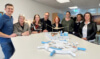 Team des Sozialunternehmens und Team vom AMS Salzburg vor dem Modell des Kreativraums.