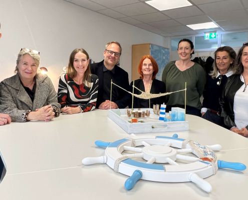 Team des Sozialunternehmens und Team vom AMS Salzburg vor dem Modell des Kreativraums.