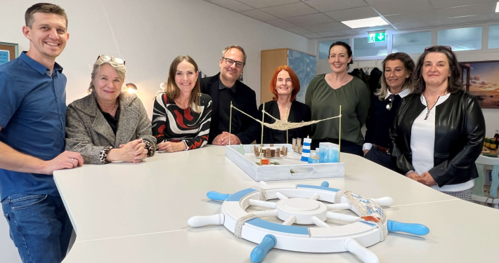 Team des Sozialunternehmens und Team vom AMS Salzburg vor dem Modell des Kreativraums.
