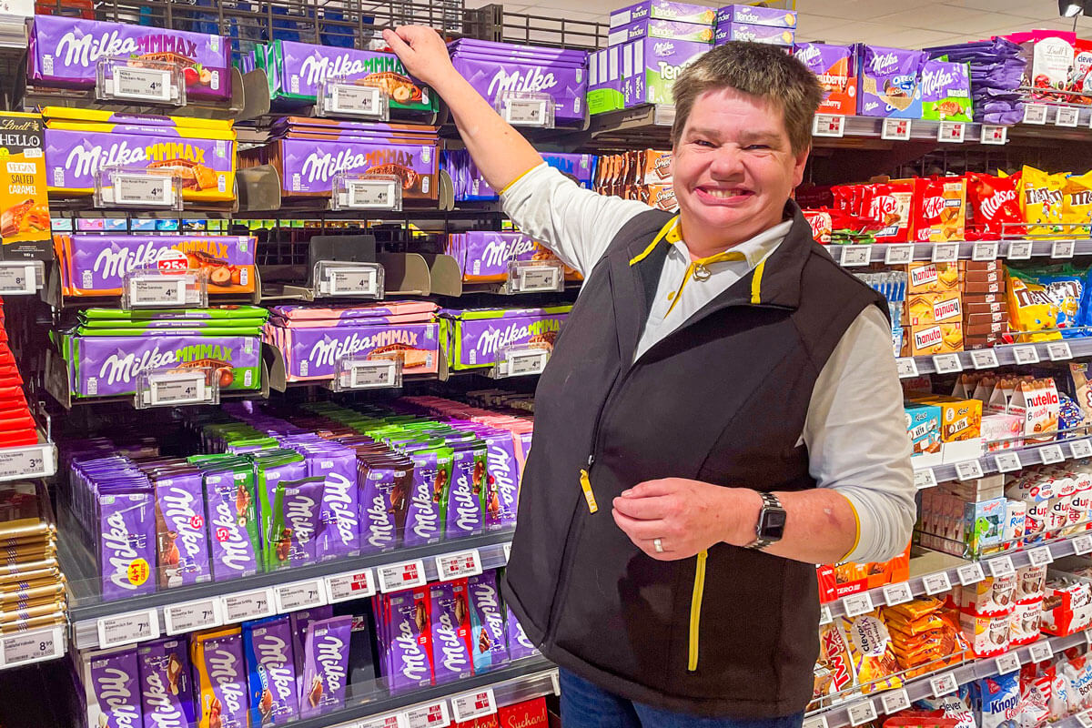 Eine lächelnde Frau schlichtet Schokolade in ein Supermarkt-Regal.