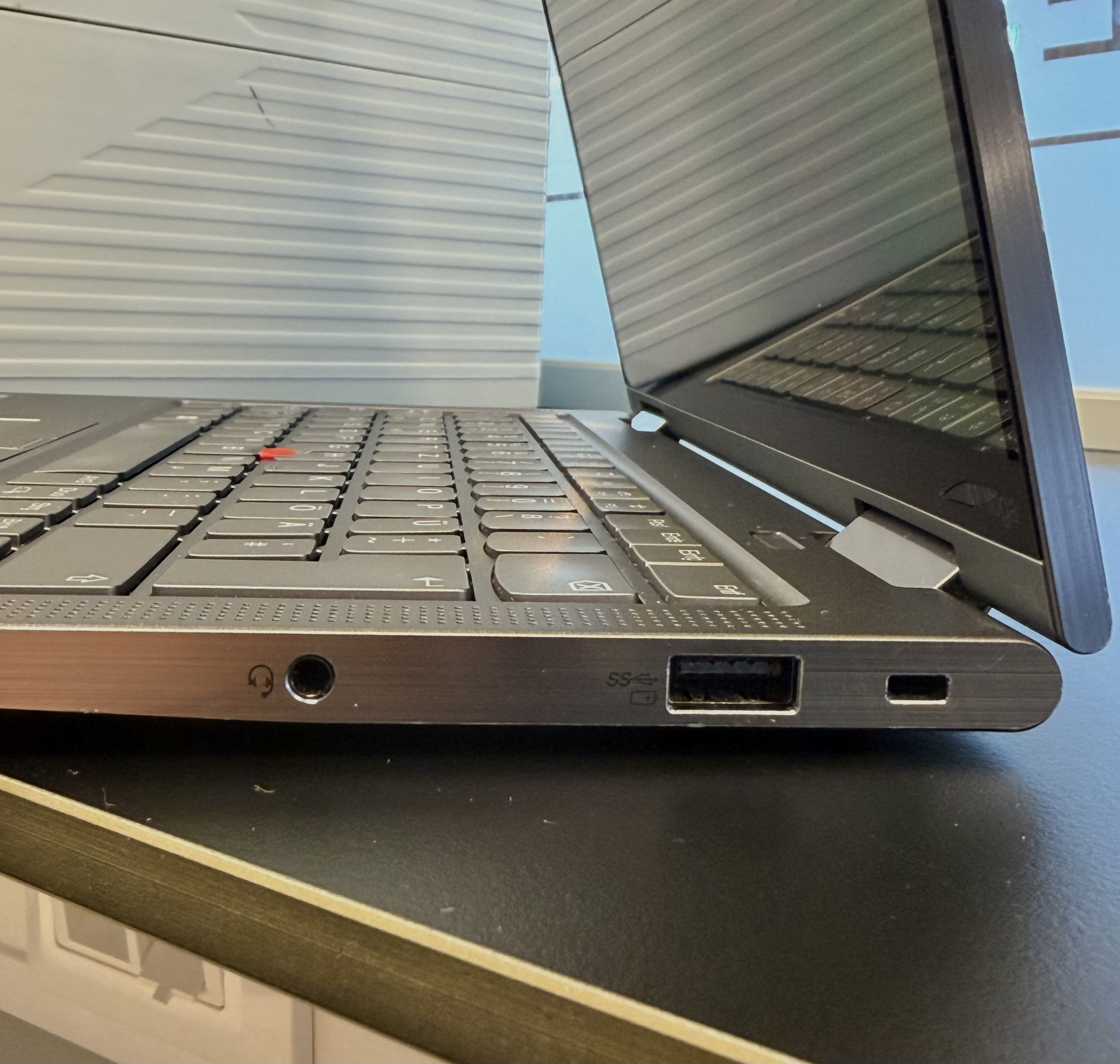 Geöffneter Laptop mit Tastatur und seitlichen Anschlüssen auf einem dunklen Tisch