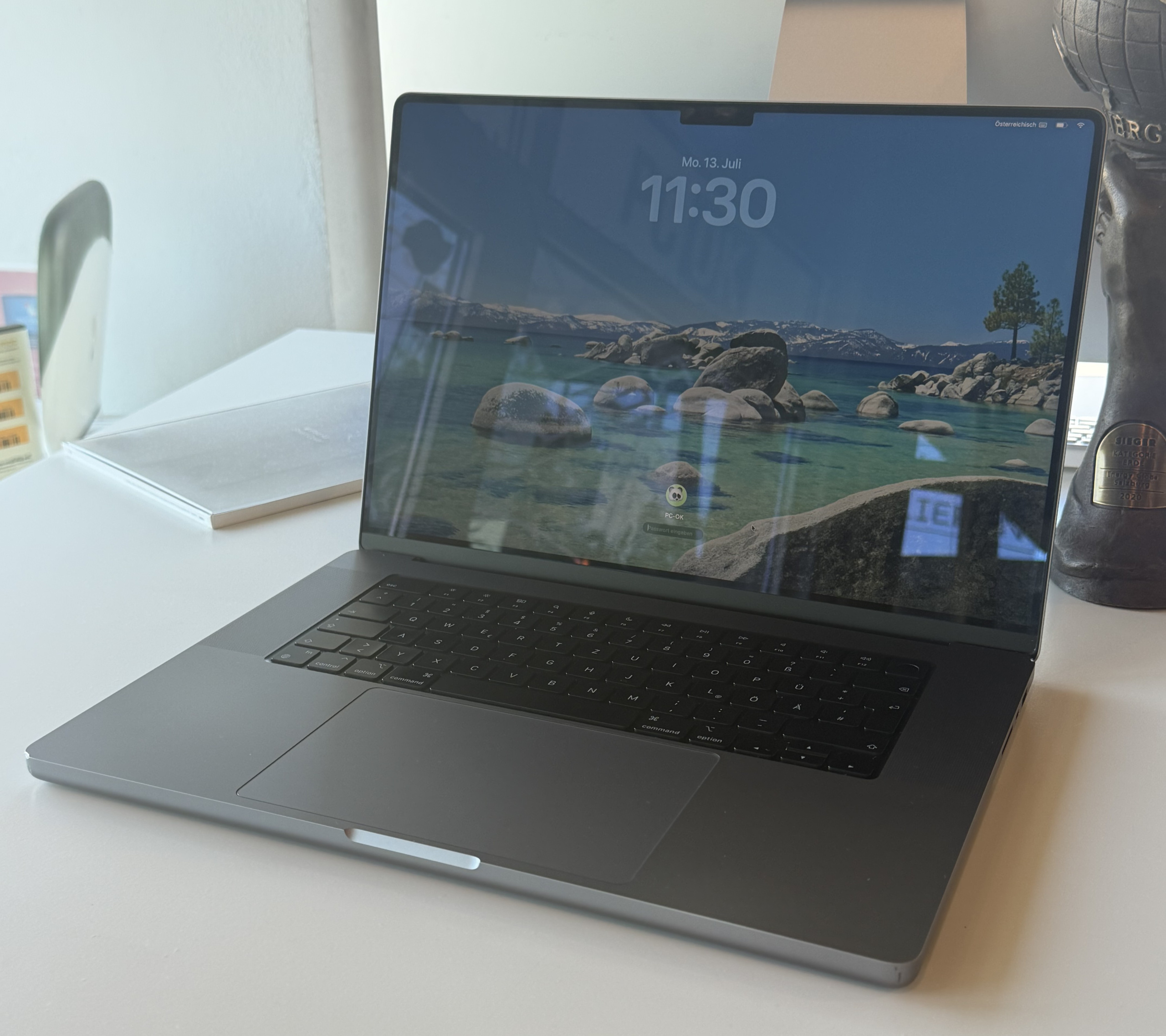Geöffneter Laptop auf einem hellen Tisch mit Sperrbildschirm und Pokal daneben